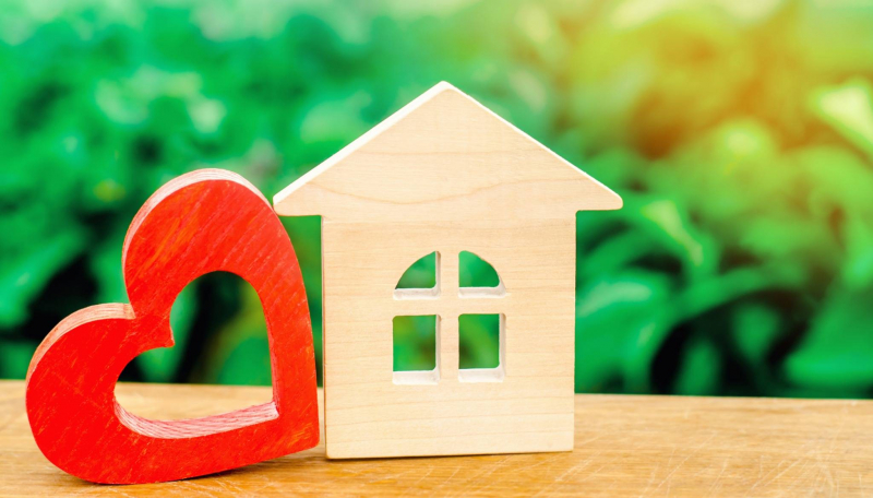 Wooden house model next to a red heart, representing homeownership and community support